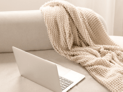 Open laptop on a neutral couch with a cozy knit blanket, representing calm, values-aligned workspaces for introverted entrepreneurs.