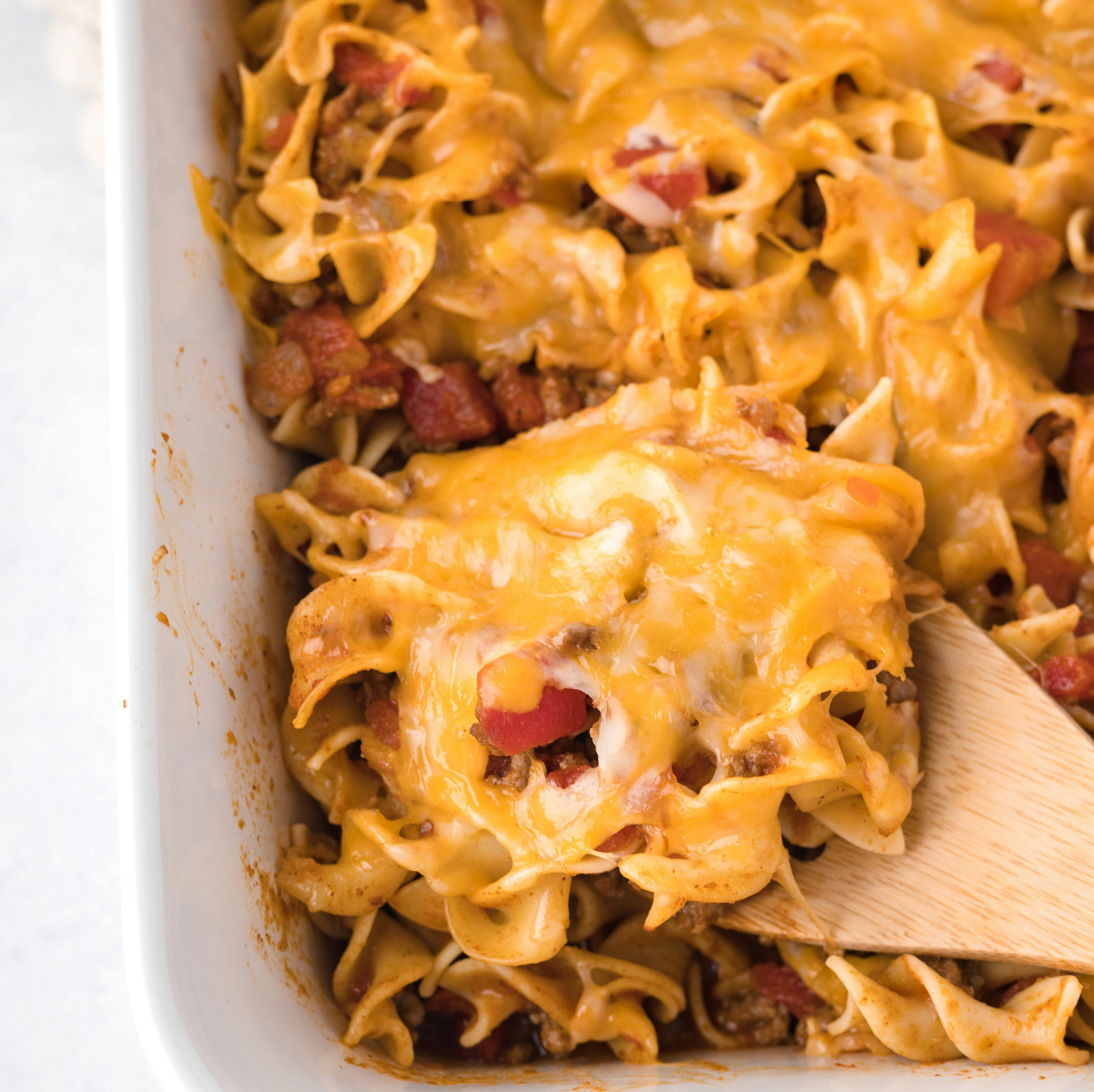 cheesy beef noodle casserole being lifted with a wooden spoon