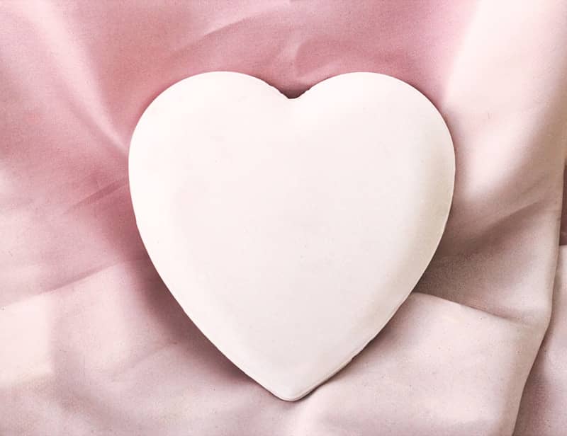 A white heart-shaped object placed on a smooth, pink fabric background.