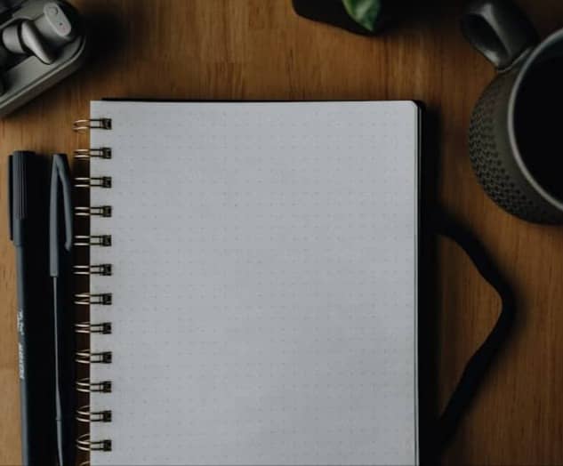 Notebook, pen, headphones, and coffee on a wooden desk.