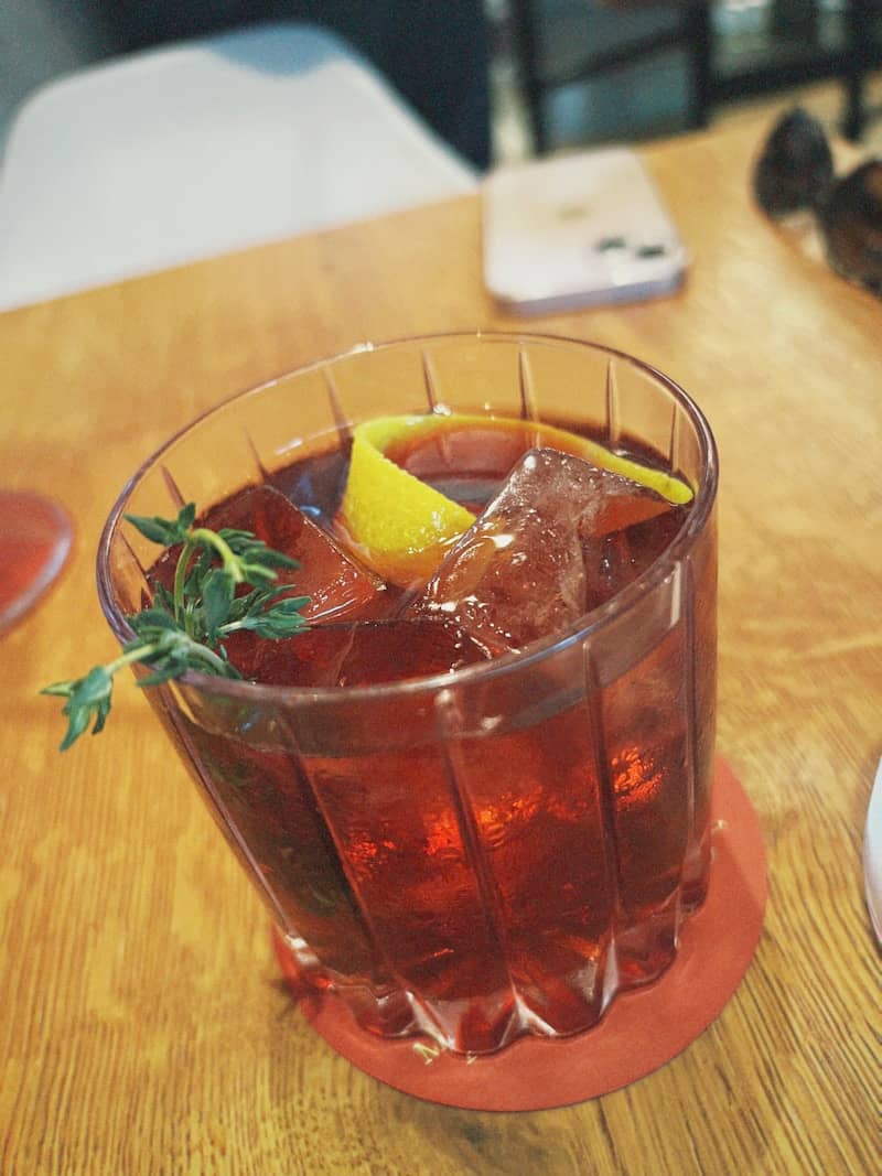 A dark red cocktail with ice and lemon garnish.