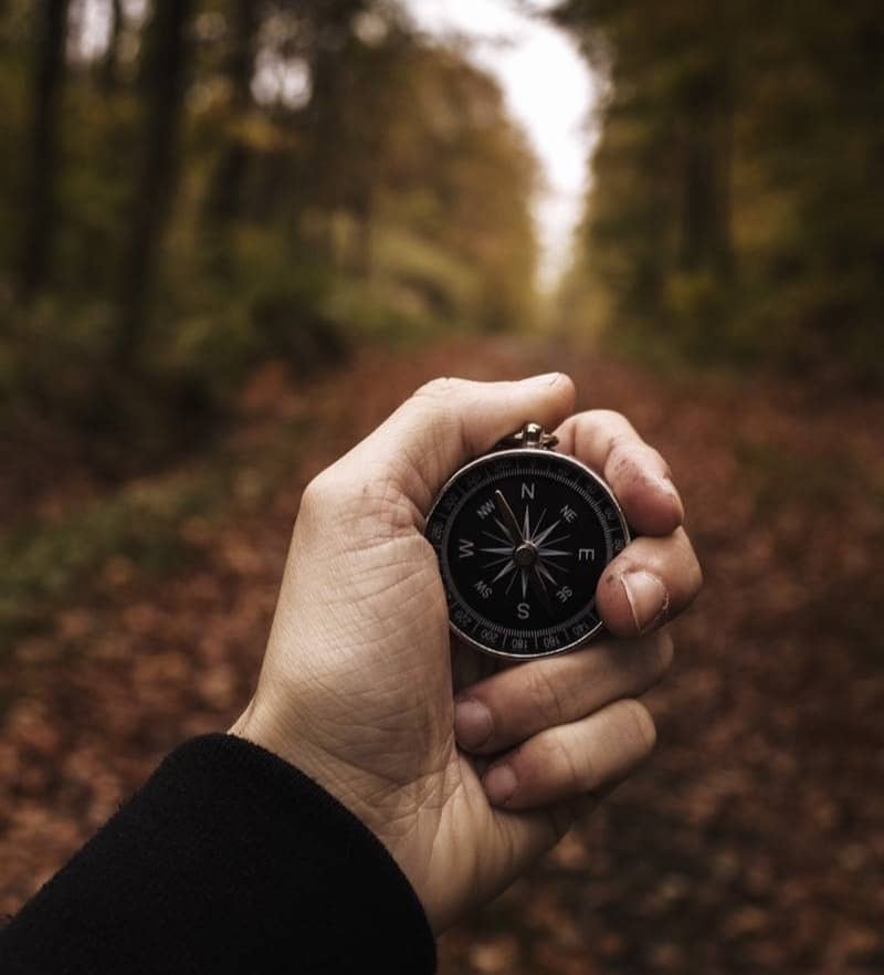 Man holding a compass along a wooded path.