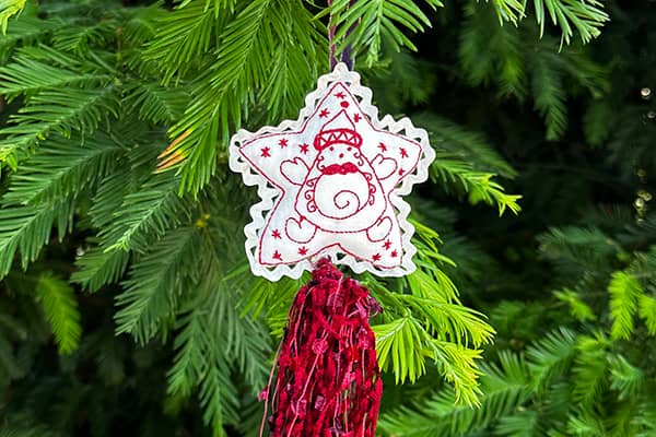 Redwork embroidered Santa Star with a rayon ric rac trim around the star shape and a tassel of red multi-textile threads and chenille yarn.