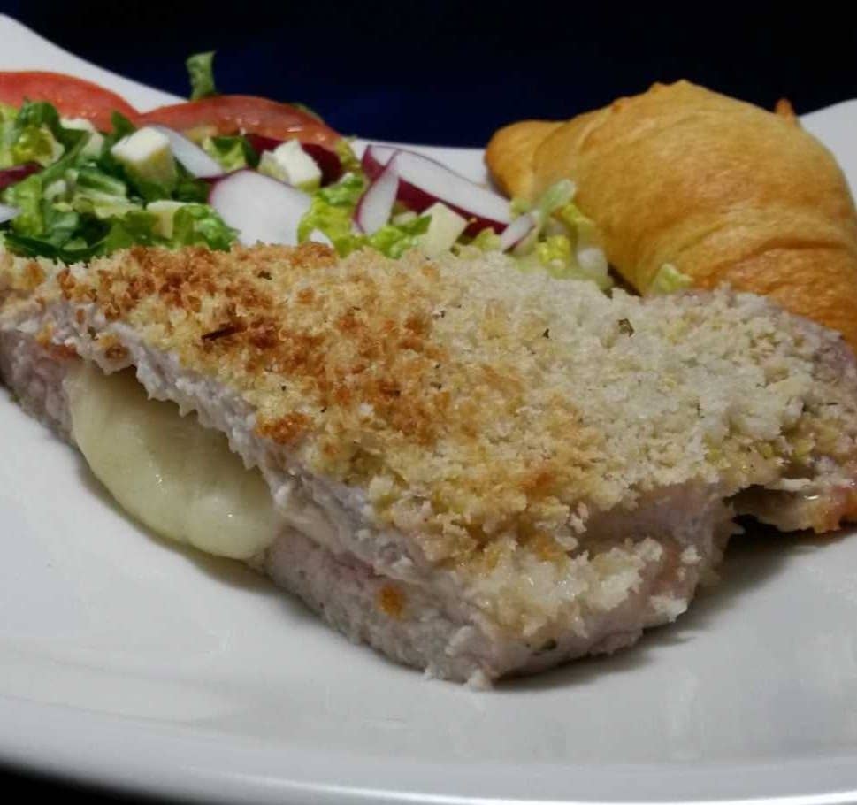 Side view of pork cordon bleu on a white polate served alongside croissant and salad.