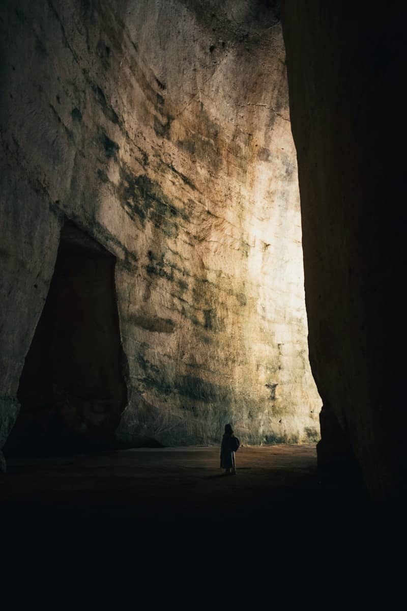 A person stands silhouetted in a vast, illuminated cave.