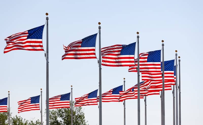 Many american flags waving on flagpoles against a clear sky.