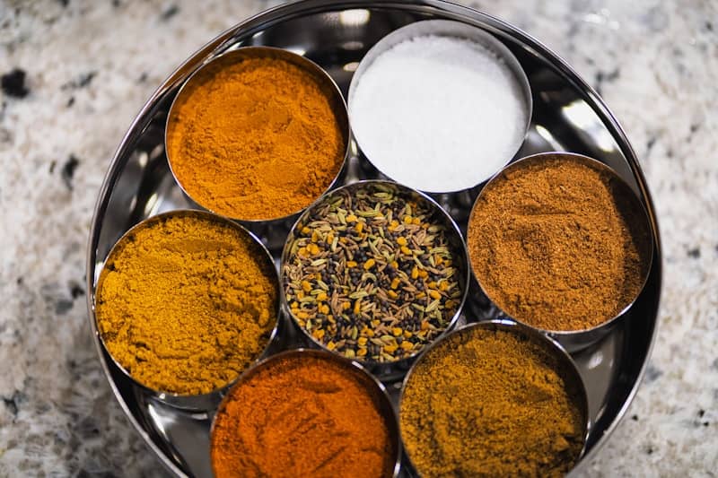 Various colorful spices arranged in metal bowls on a tray.