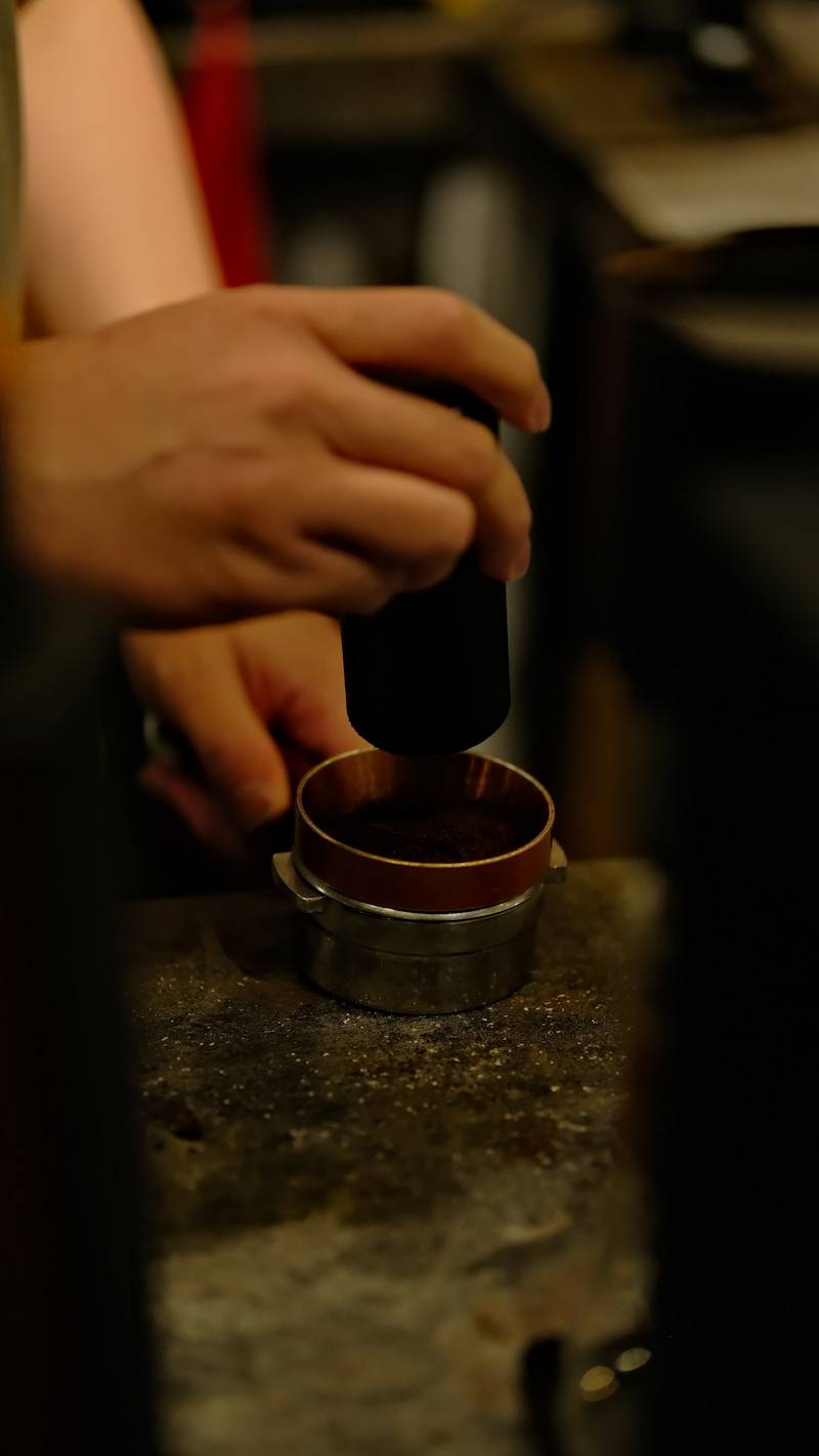 A person tamps coffee grounds into a portafilter.