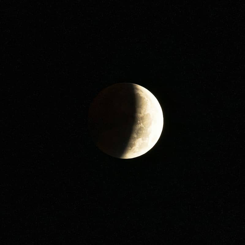 A partially illuminated moon against a dark starry sky