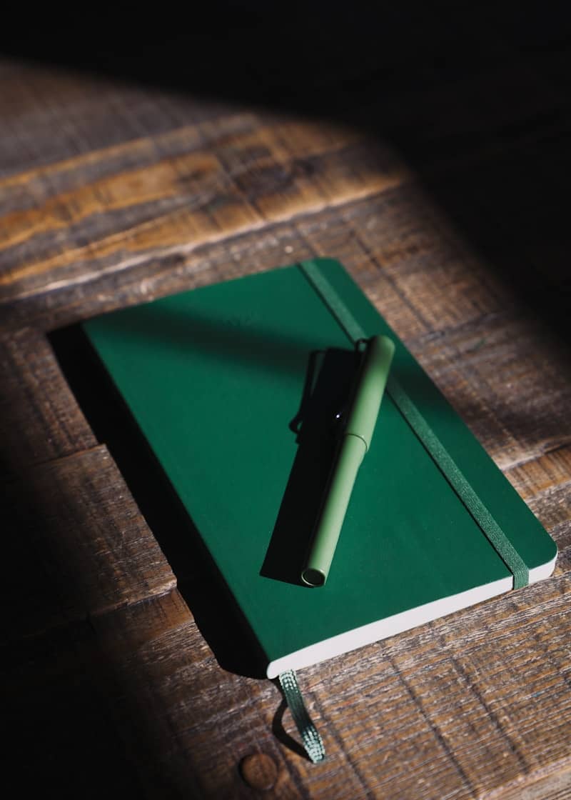 Green notebook and pen on a wooden surface.