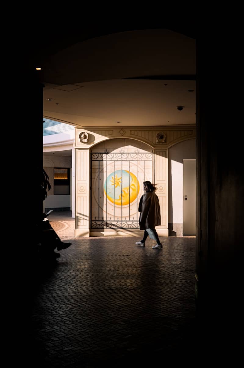 A person walks through a sunlit archway.