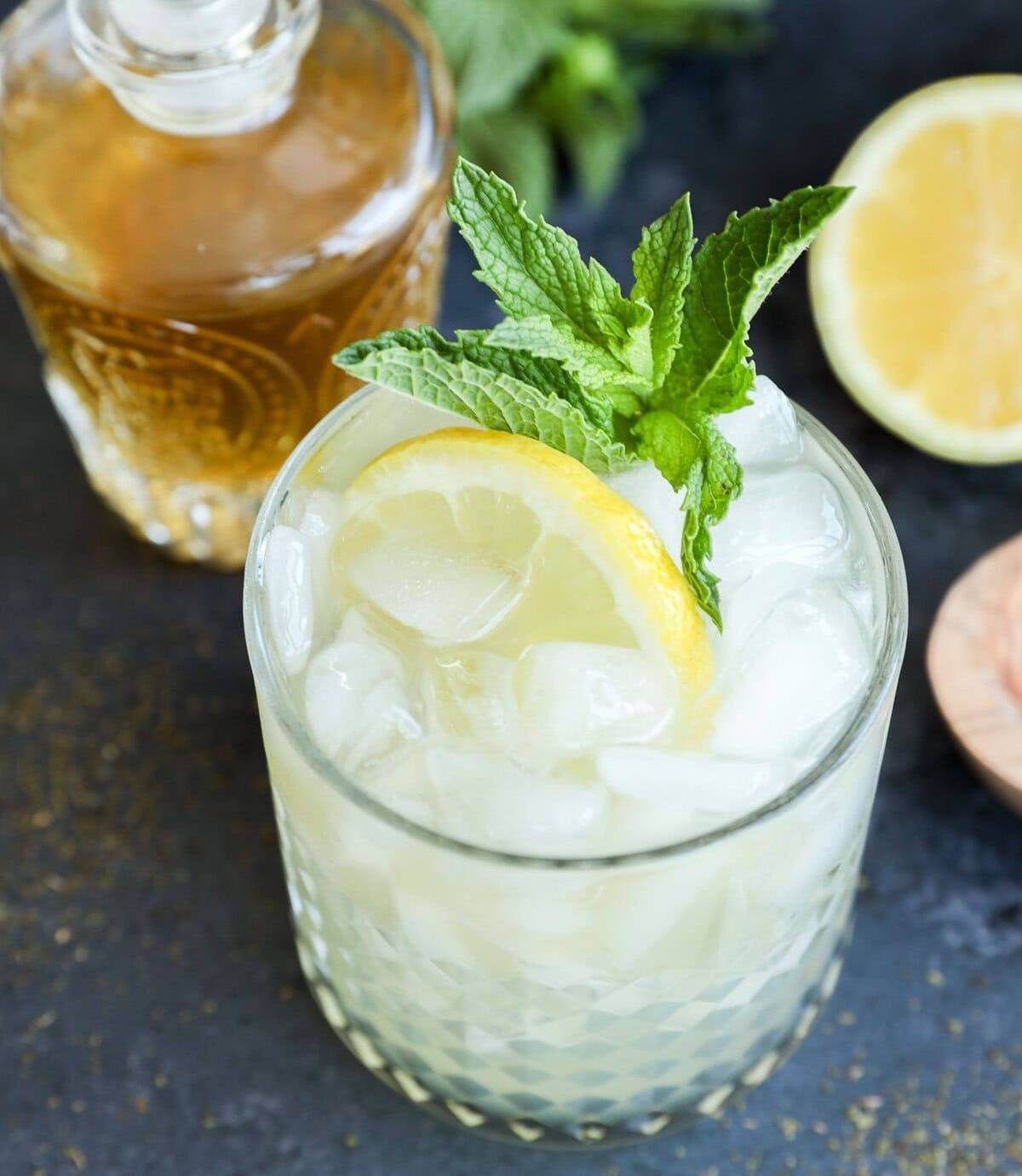 Overhead view of a pale yellow cocktail garnished with a lemon wheel and sprig of mint.