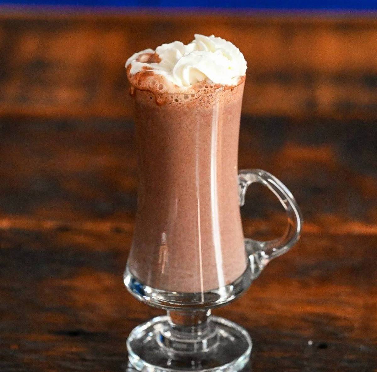 A tall glass mug holds hot chocolate topped with whipped cream.