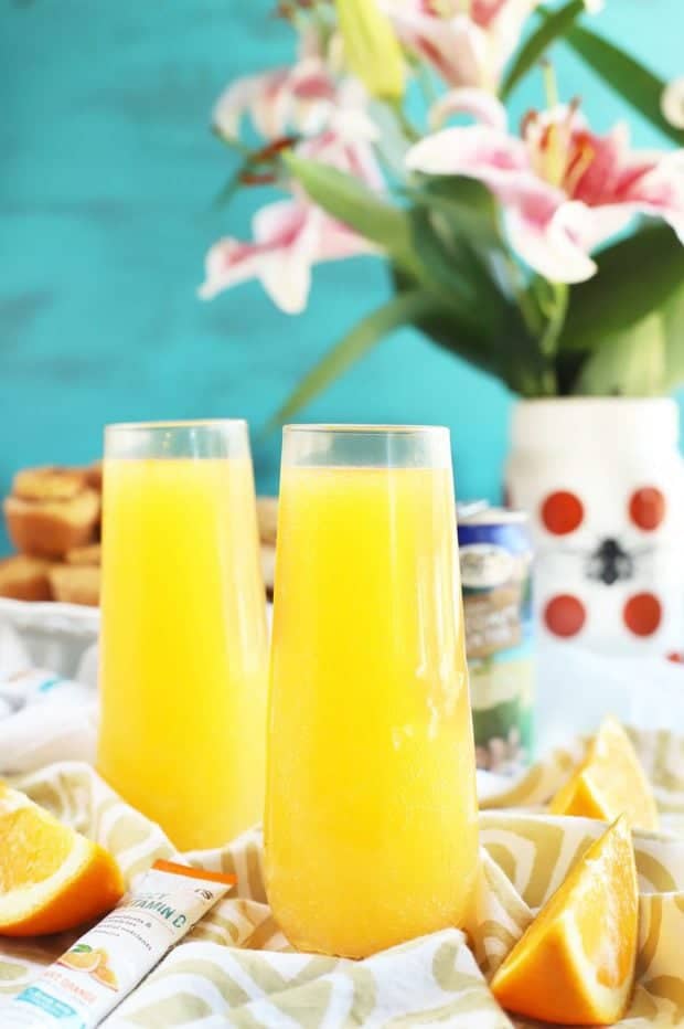 Two orange juice drinks on a table set for brunch.