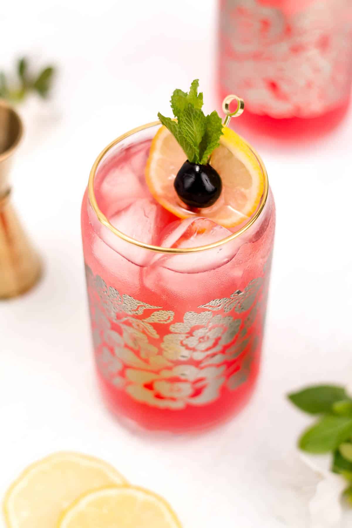 A pink drink in a glass with a lemon round and cherry.