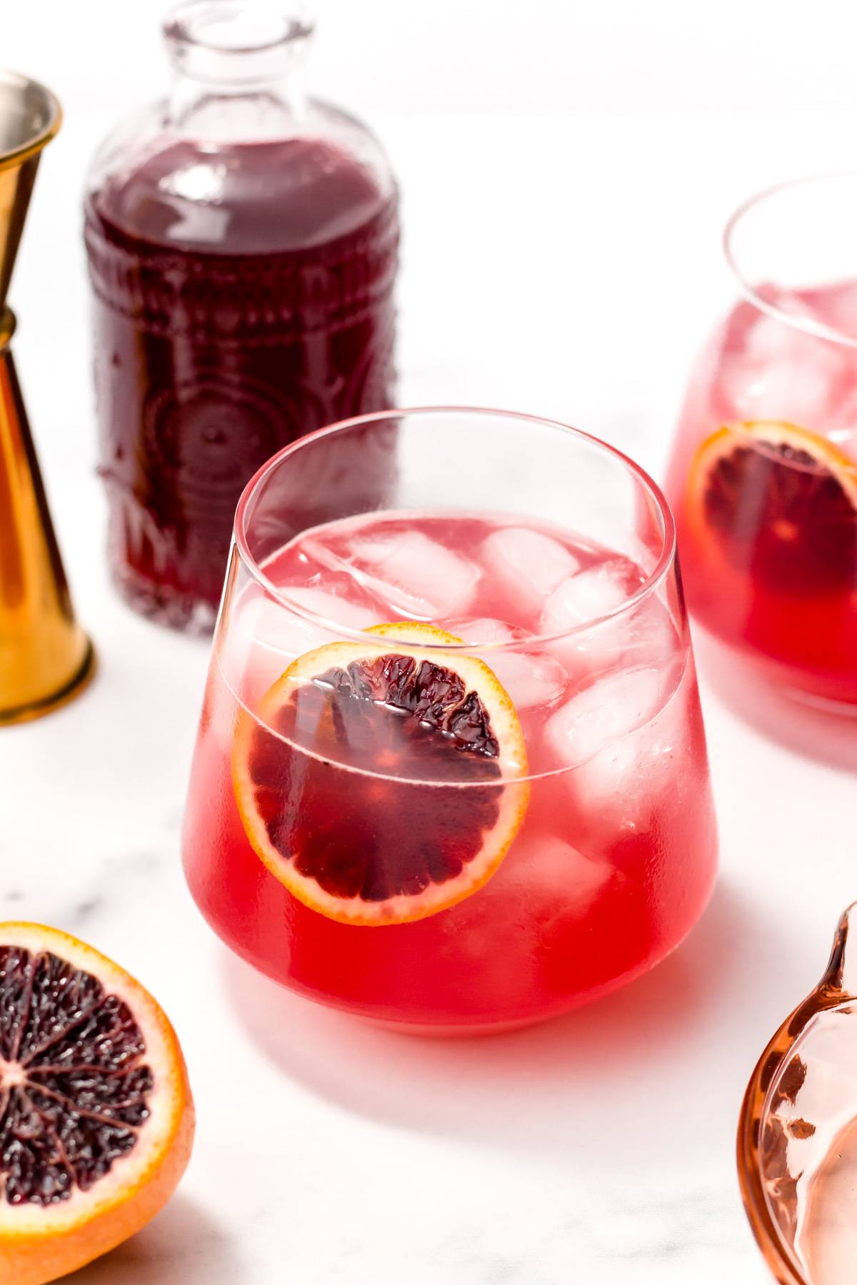 A red drink in a stemless glass with ice garnished with a blood orange round.