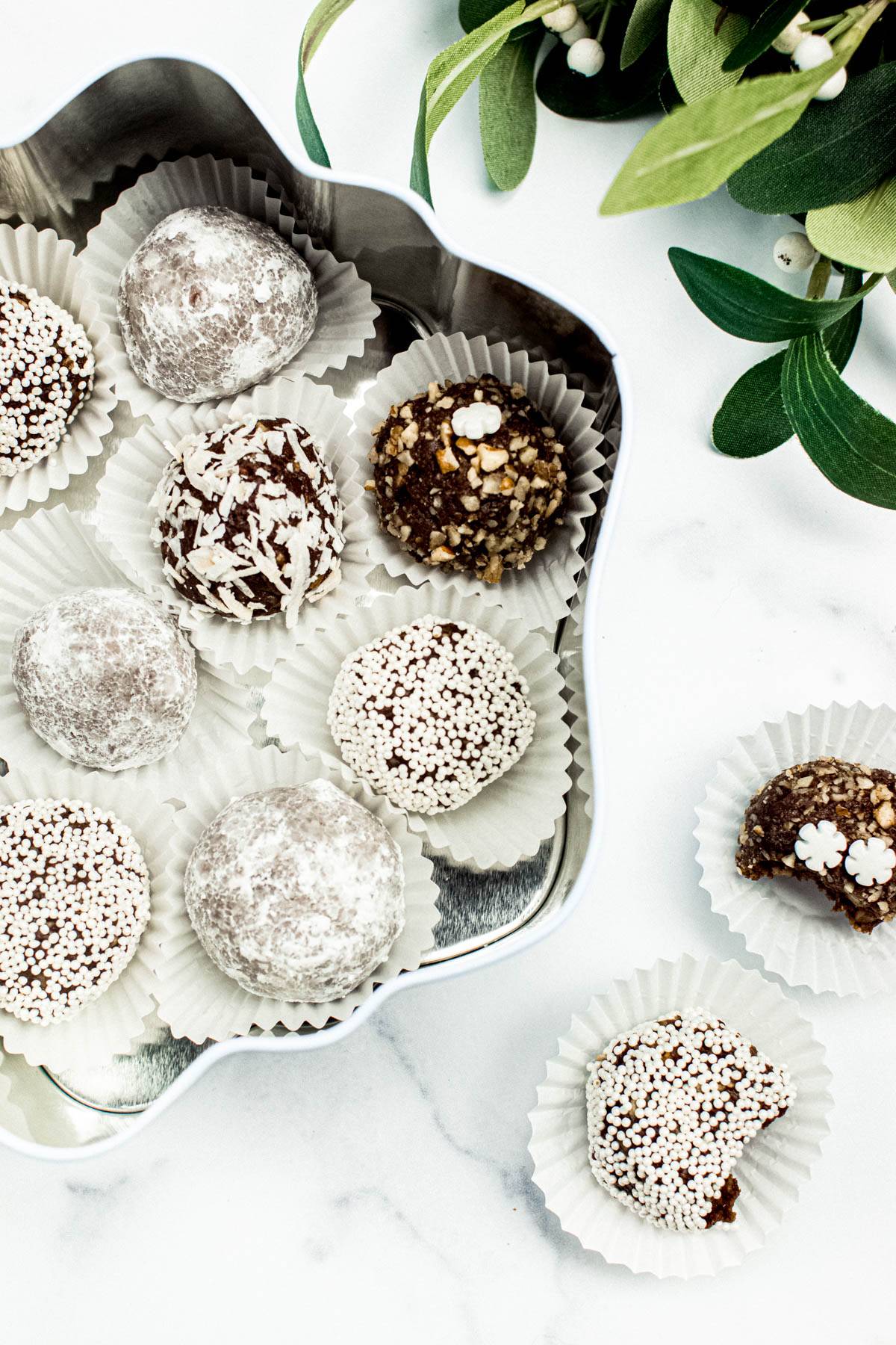 Cookie balls in a silver tin sit near greenery.