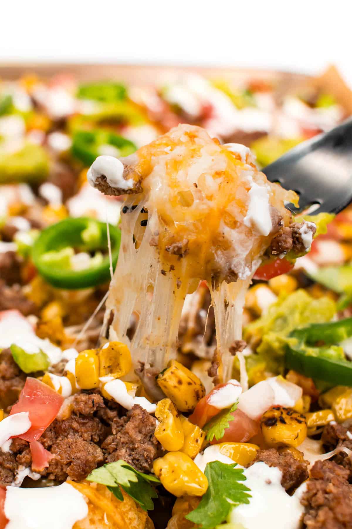 A fork scoops up a bite of totchos covered in cheese.