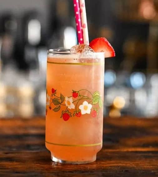 A pink drink in a glass with a strawberry pattern around the middle.