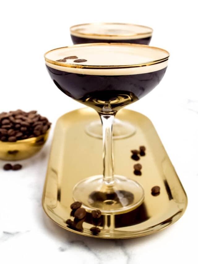 Two brown cocktails in stemmed glasses on a gold oval tray.