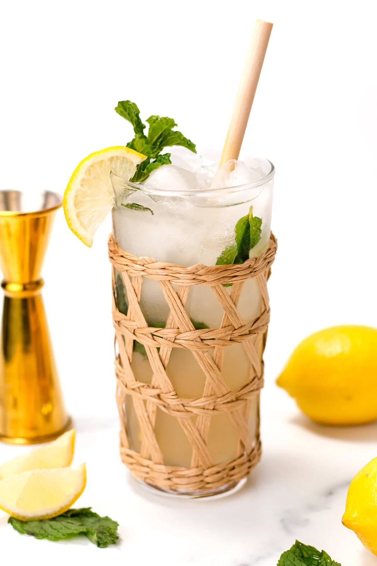 A glass with a rattan wrapping with a mint sprig and lemon wedge.