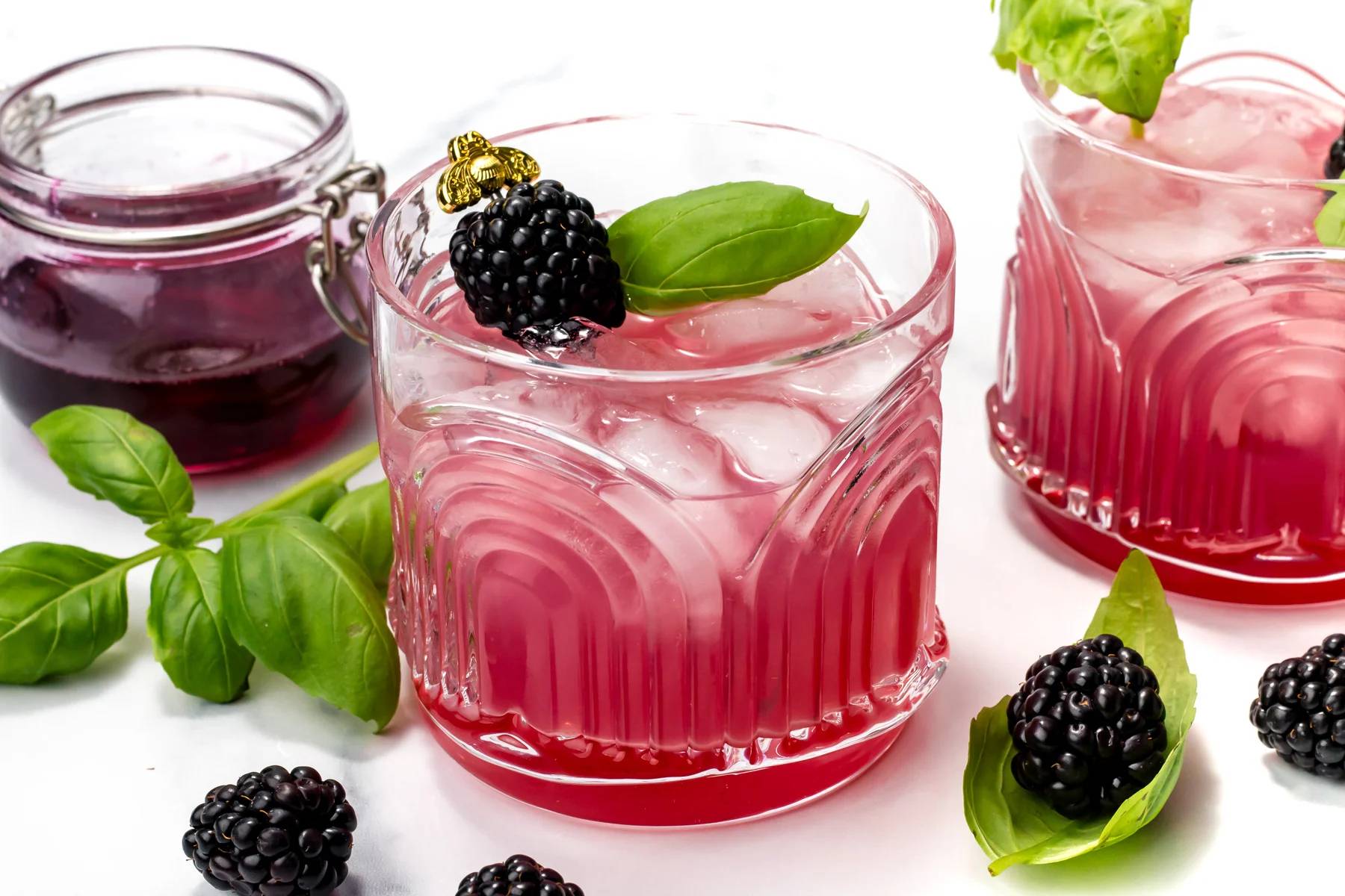 A deep red drink garnished with a blackberry on a gold bee cocktail pick.