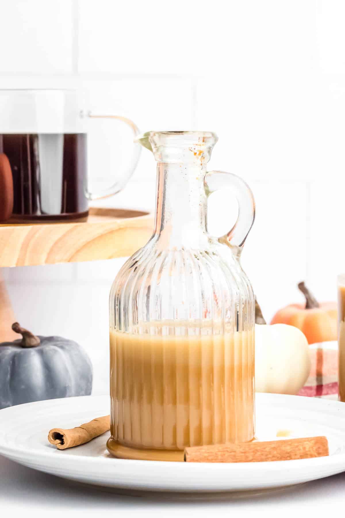 A decorative pitcher of light amber coffee creamer sits near small pumpkins.