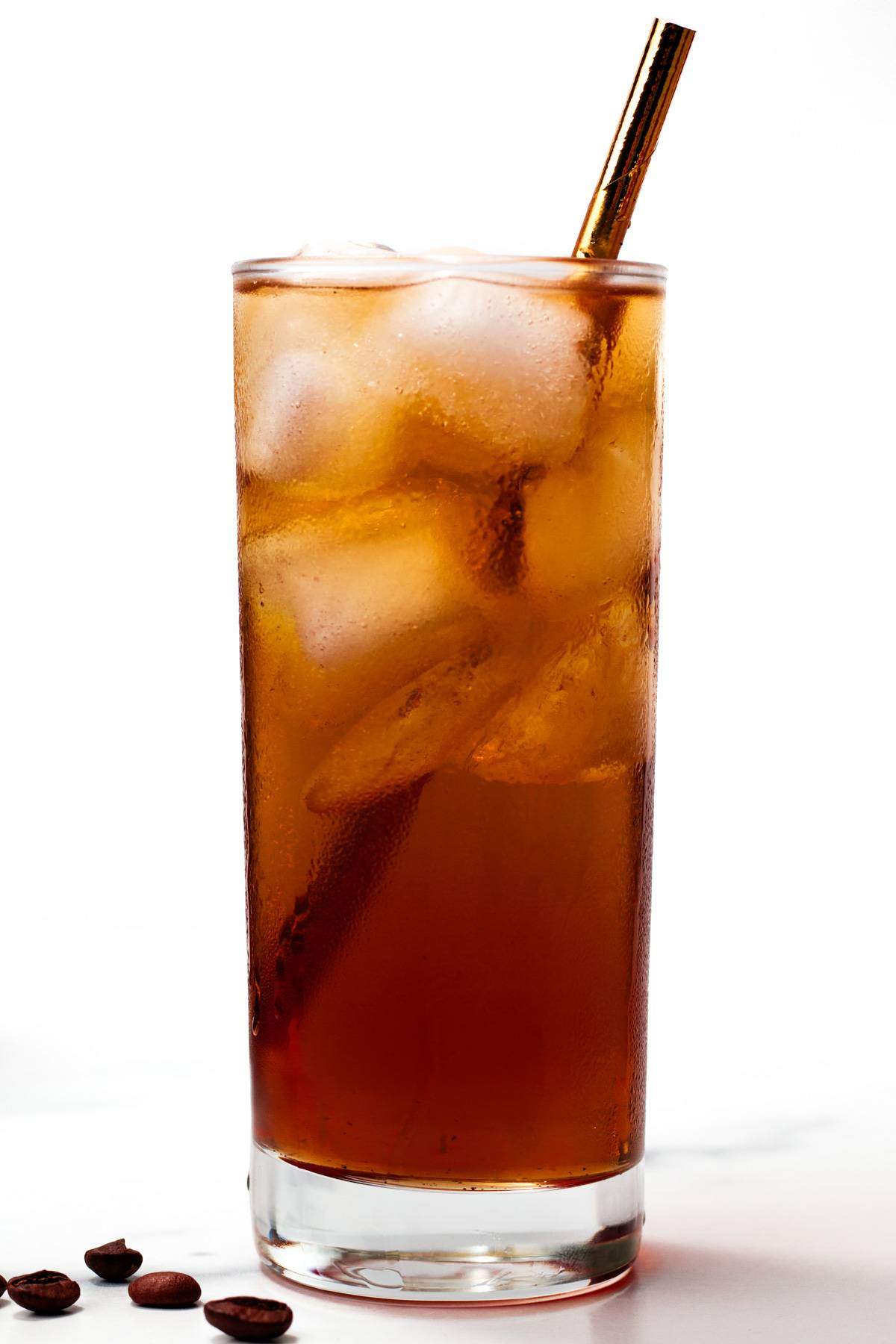 An amber iced coffee drink in a clear glass with a bronze straw.