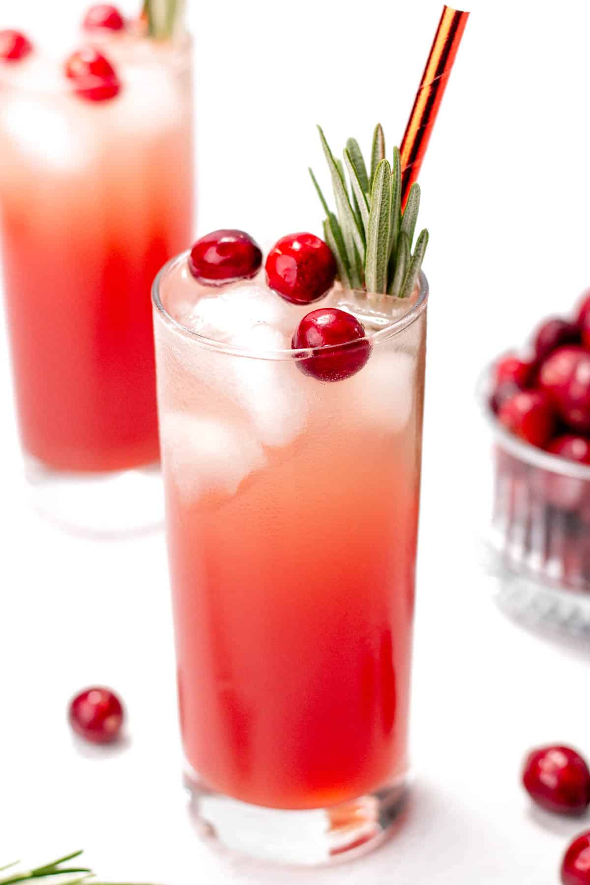 A red drink garnished with whole cranberries and a rosemary sprig.