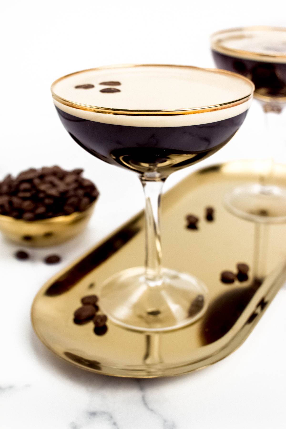 Two brown cocktails in stemmed coupe glasses on a gold oval tray.
