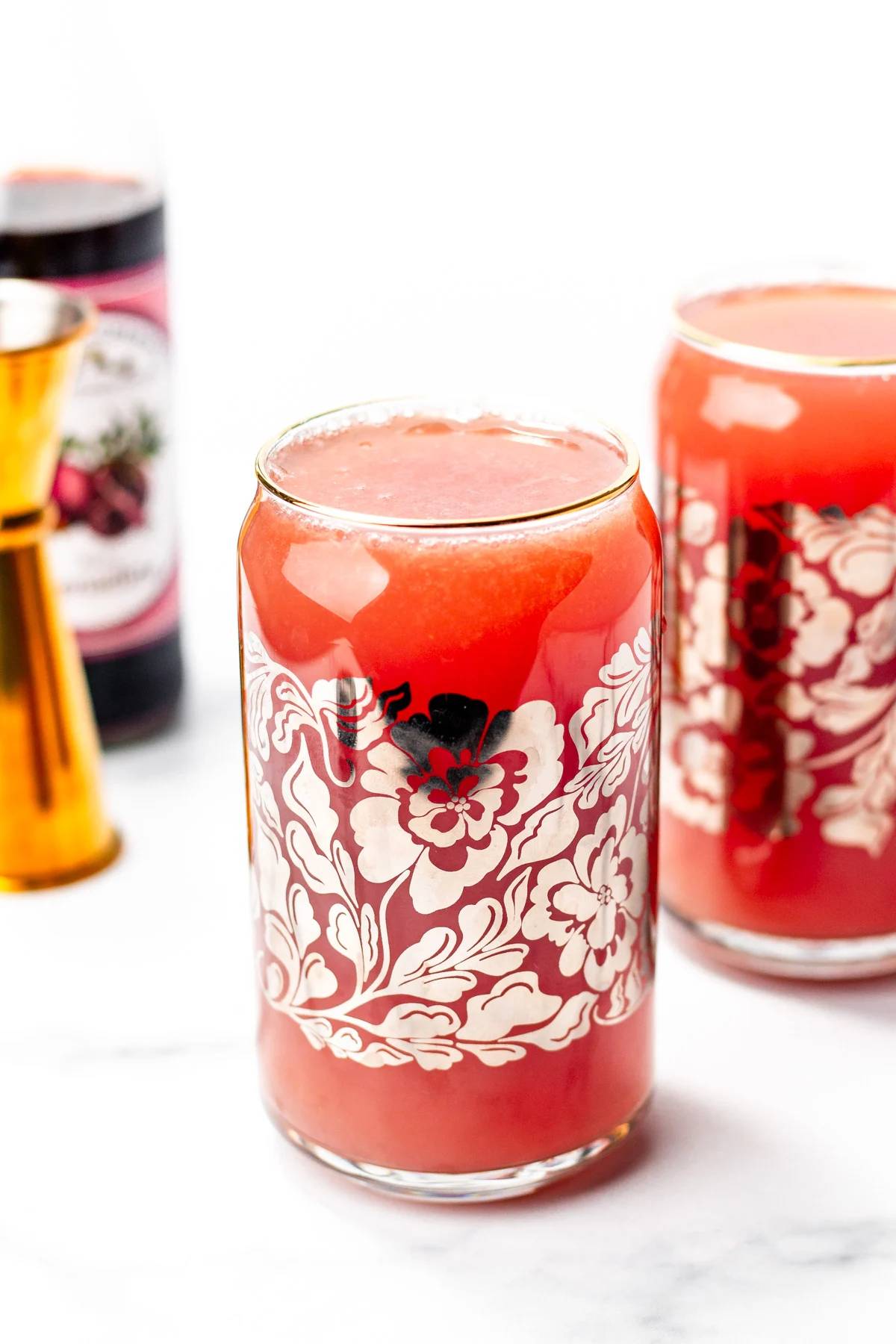 A red drink in a can glass with silver flowers on the outside.