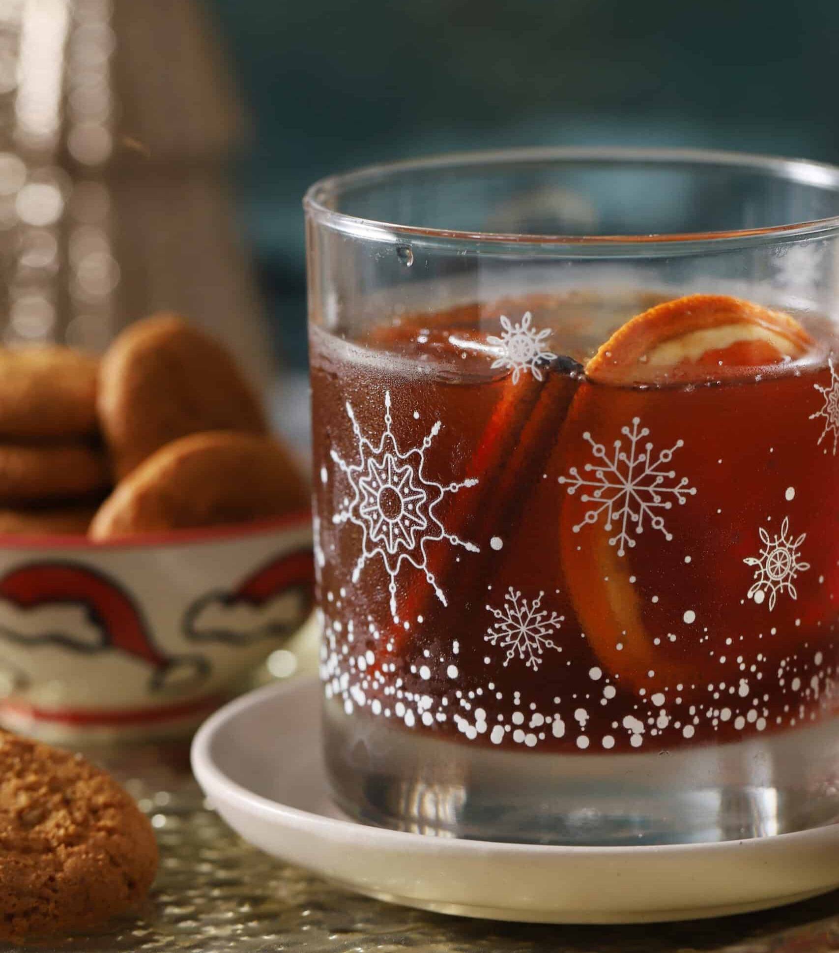 A rocks glass with white snowflakes holds an amber cocktail.