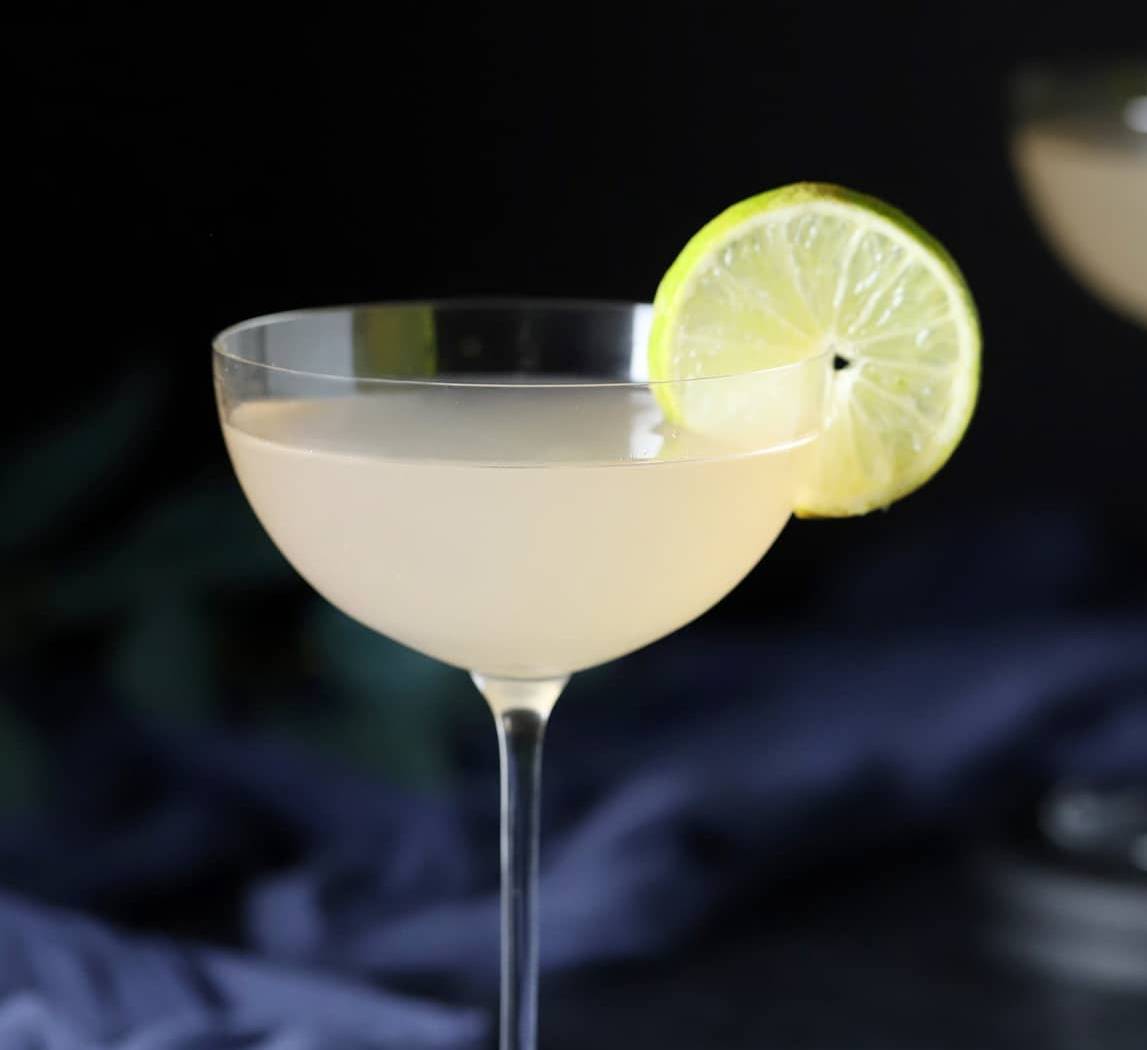 A pale drink in a stemmed glass with a lime round on the rim.