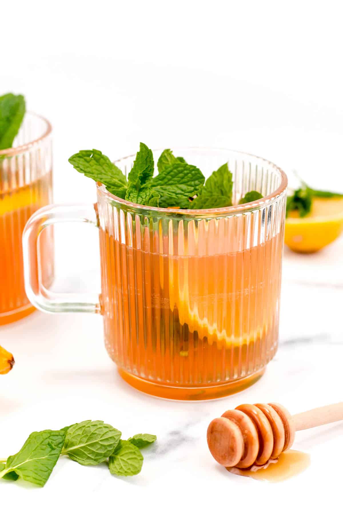 A clear mug holds an orange drink with a lemon round and mint leaves.