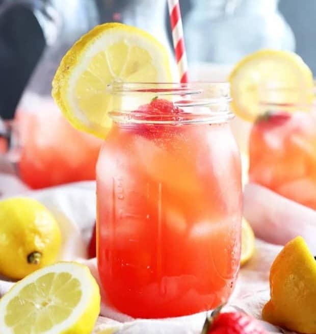 A red drink in a mason jar with a red and white striped straw and a lemon wheel on the rim.