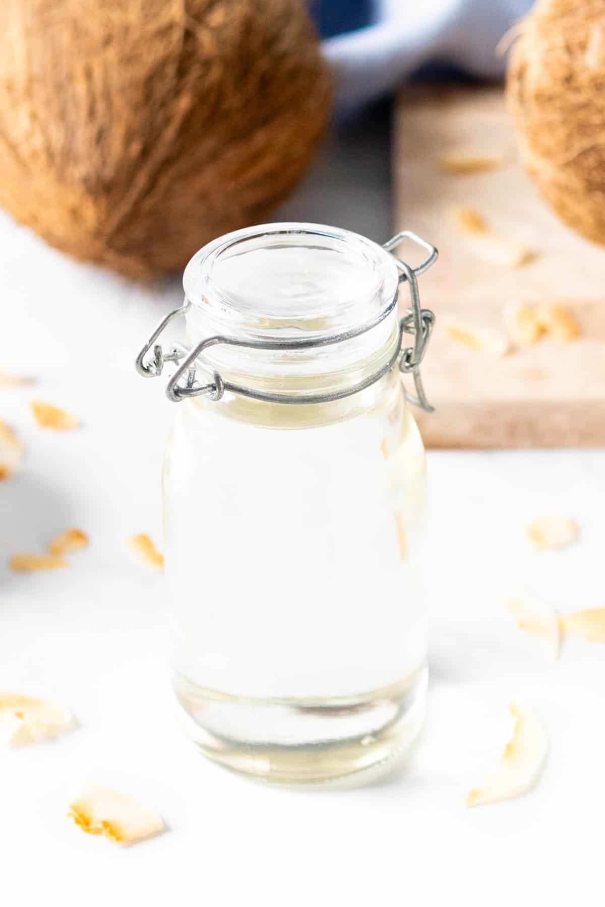 A clear bottle with a lid holds simple syrup near coconut shavings and a whole coconut.