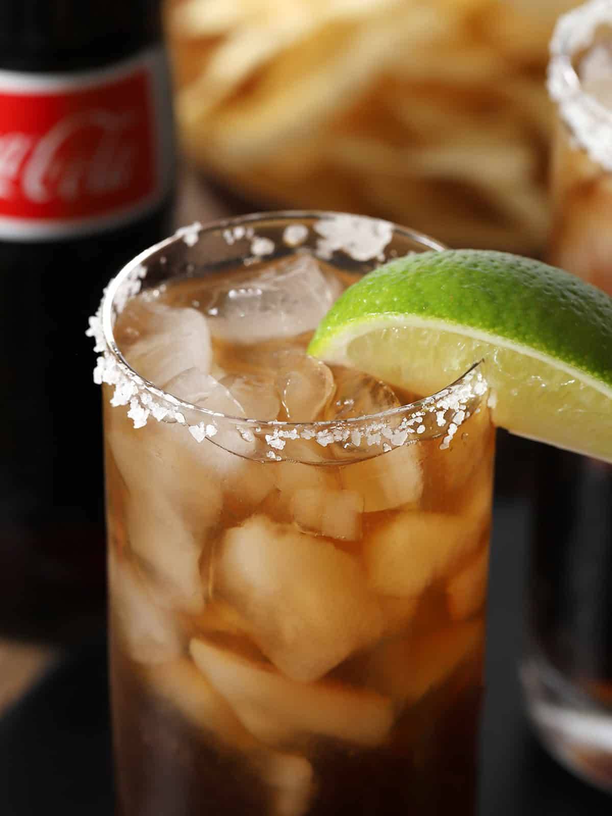 A dark cola drink with a salted rim and a lime wedge.
