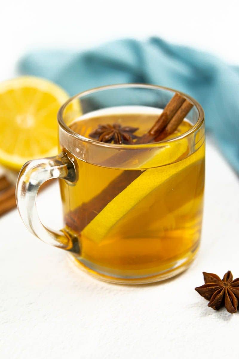 A clear mug holds an amber liquid with a cinnamon stick, star anise and lemon round.