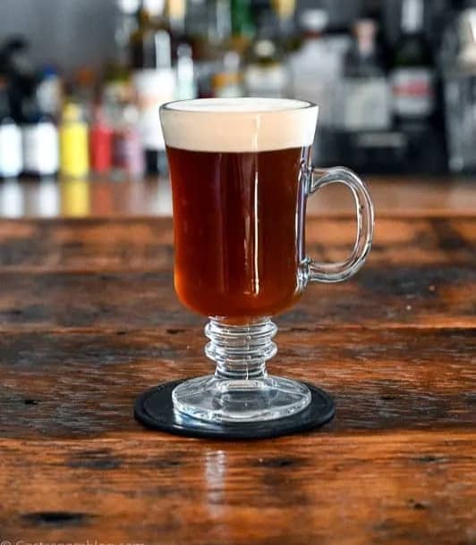 A glass mug with an amber drink sits on a wooden surface.