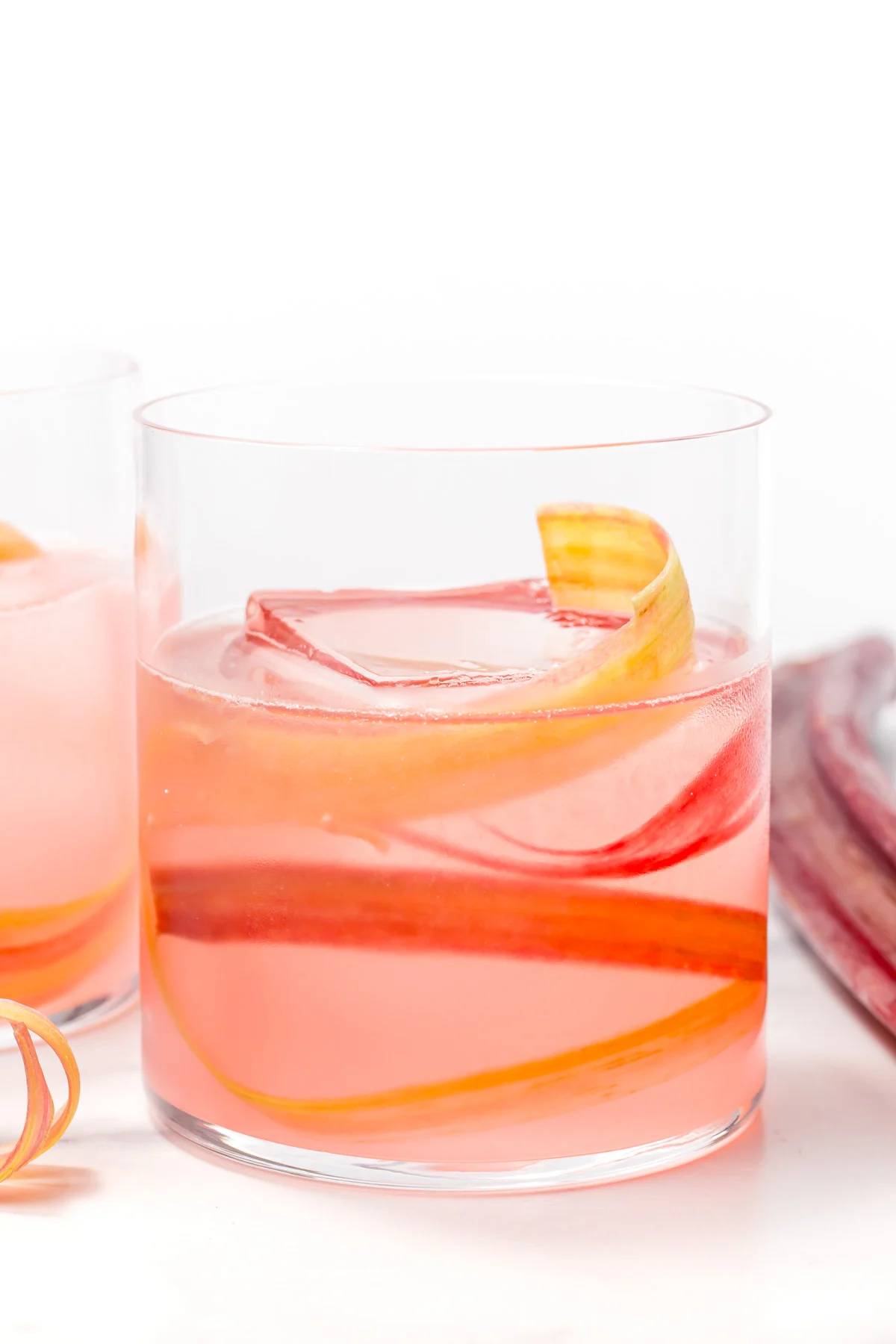 A pink cocktail with a rhubarb strip in a rocks glass.