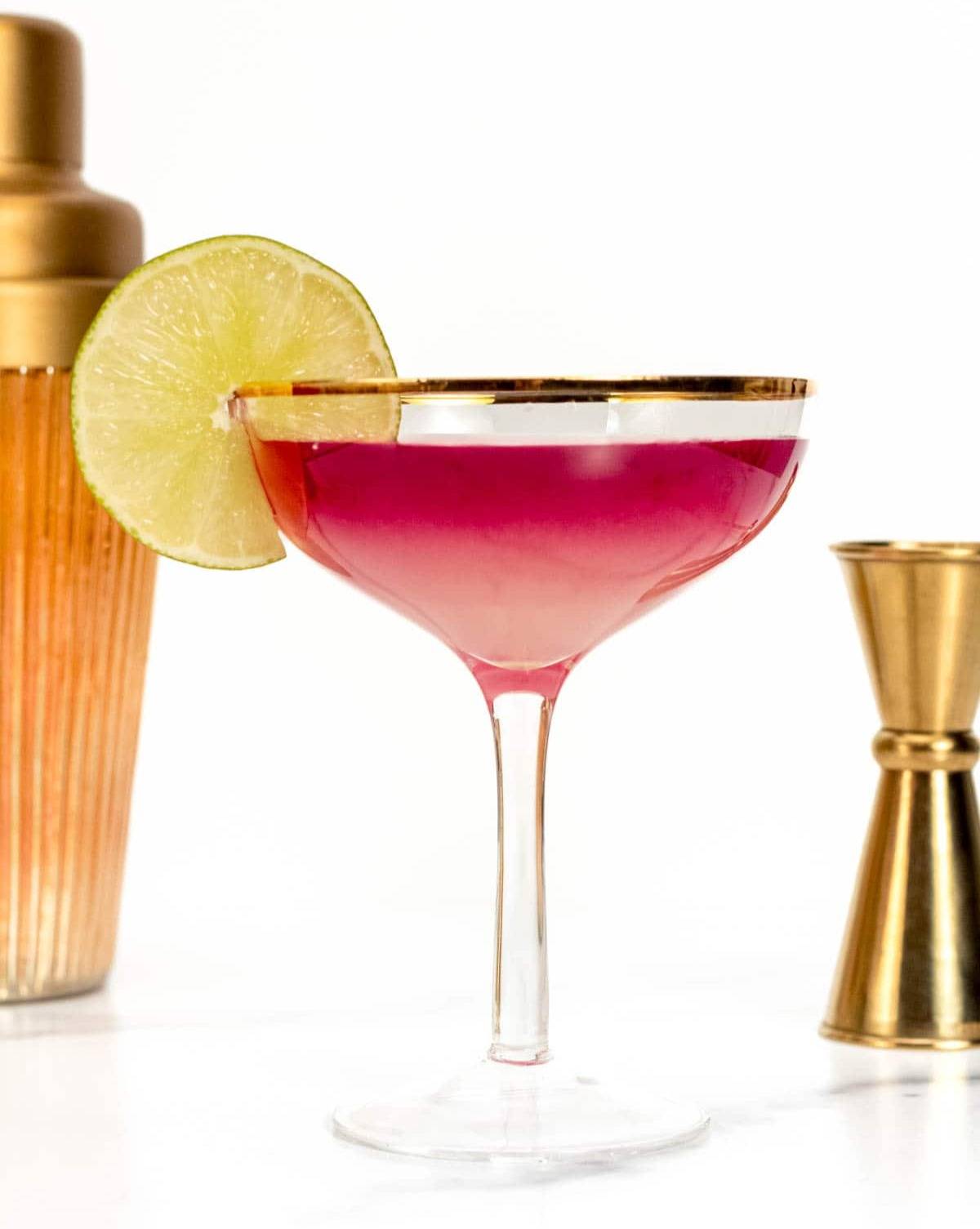 An ombre red drink in a stemmed glass with a lime wedge on the rim.