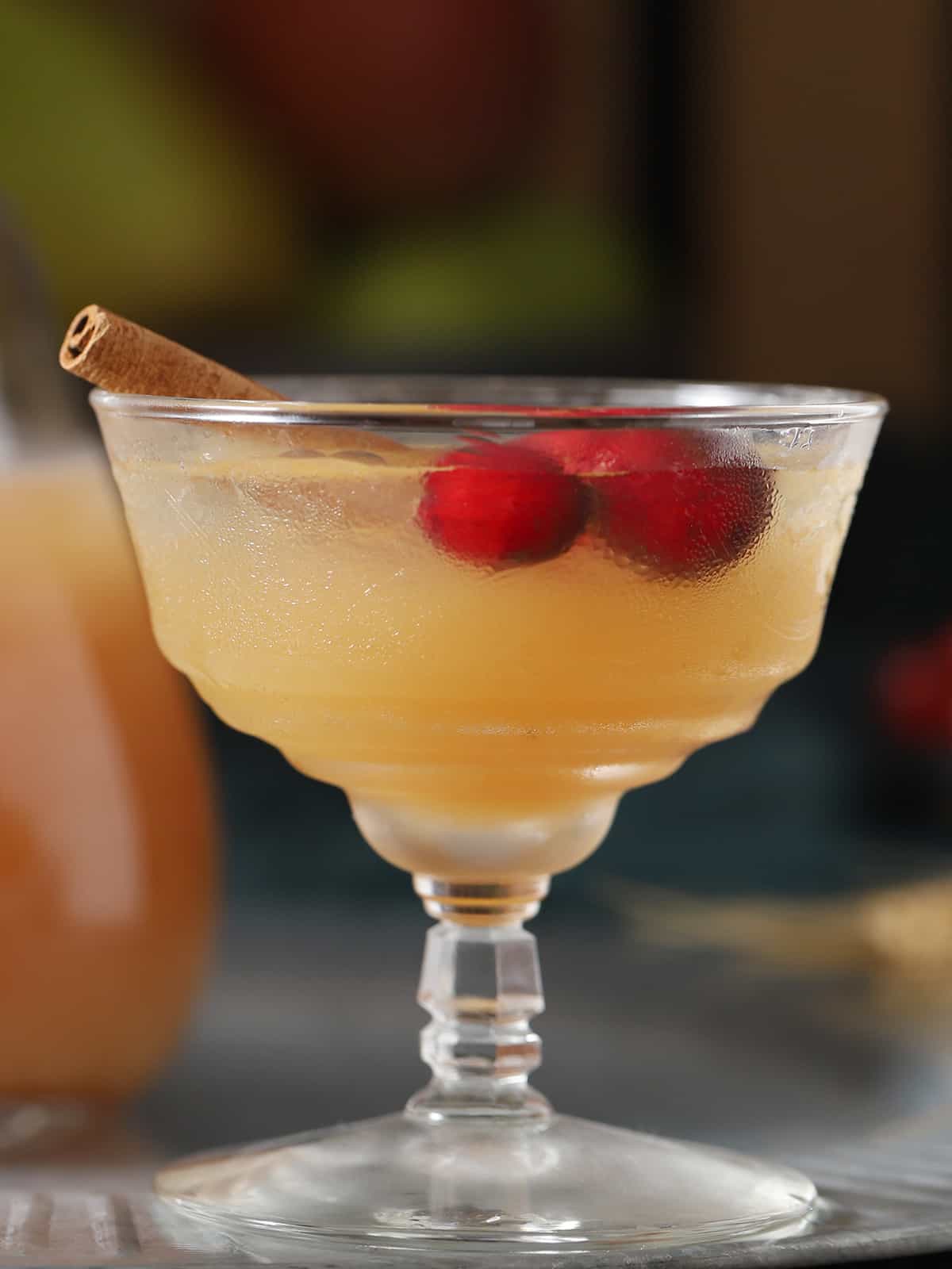 A glass with a stem holds a cocktail garnished with red berries and a cinnamon stick.