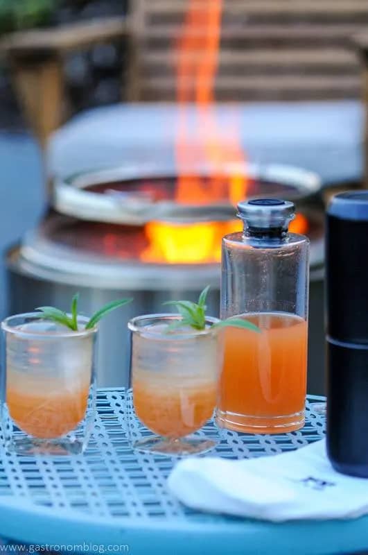 Two rum cocktails sit in front of a fire pit.