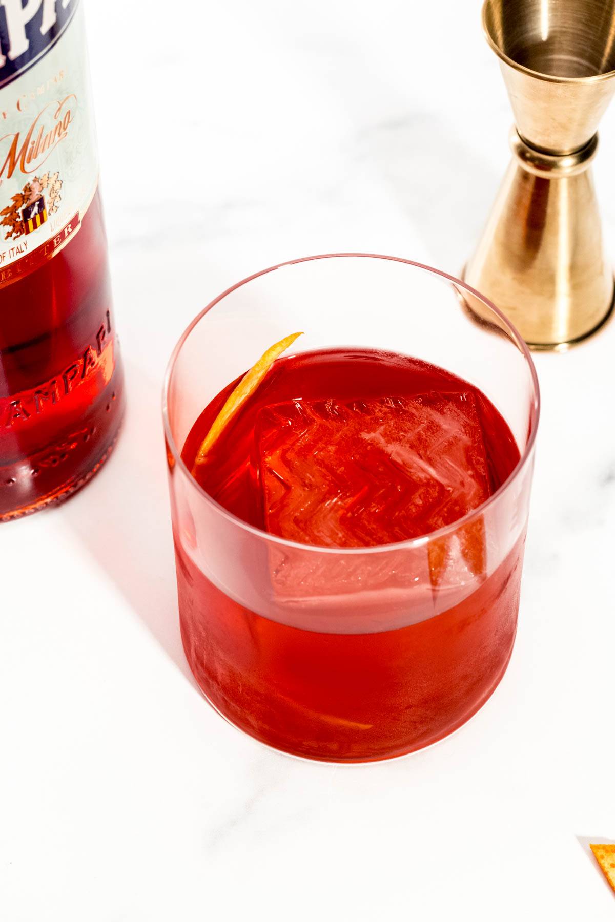 A red cocktail with a large ice cube.