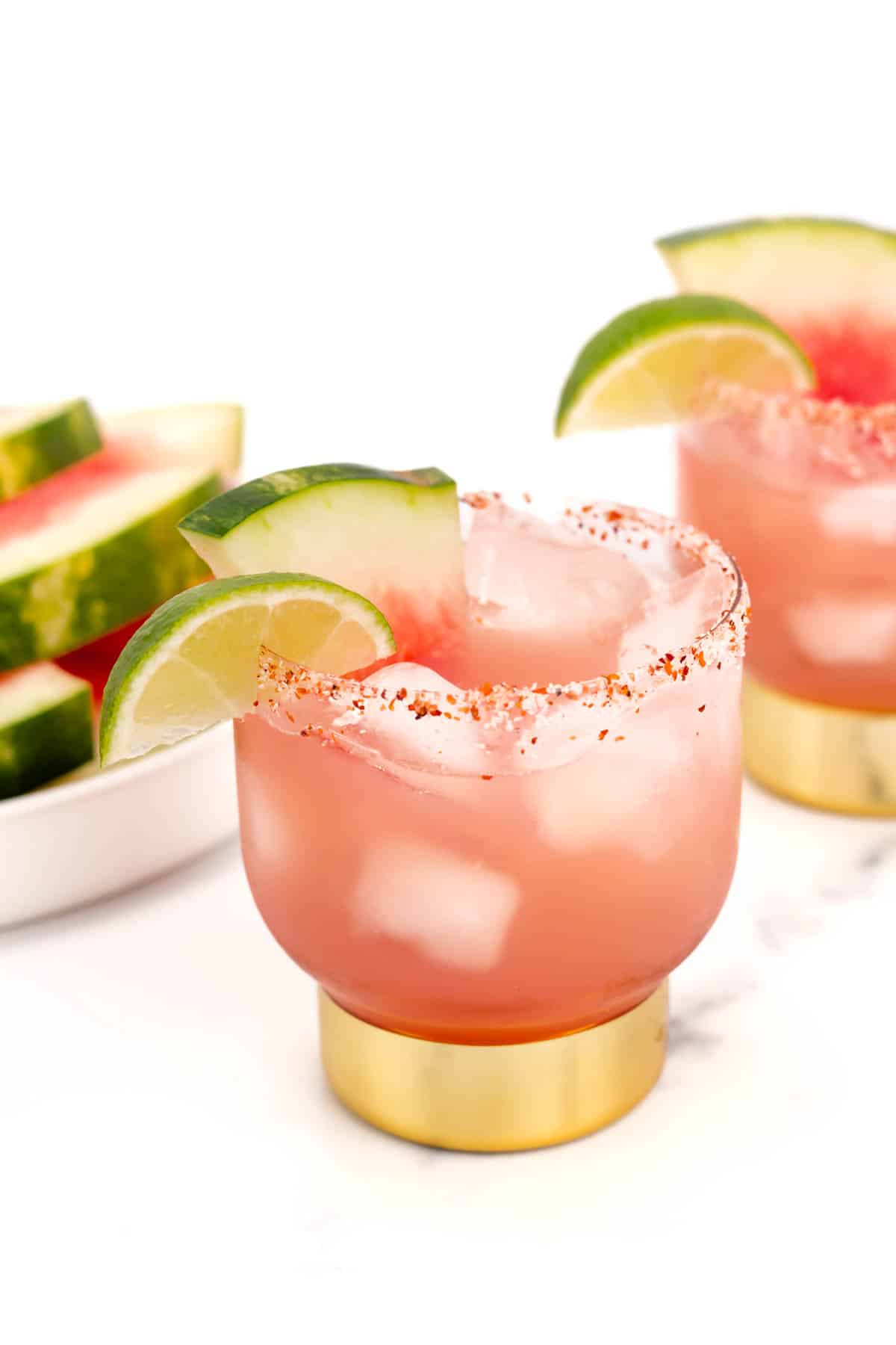 A pink watermelon margarita in a glass with a salt rim and a slice of lime and watermelon as a garnish.