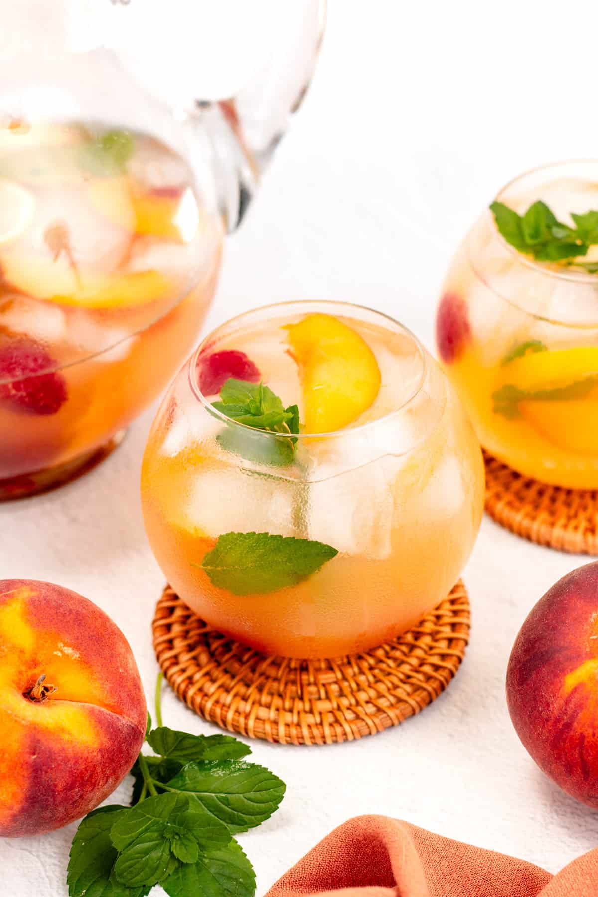 An orange sangria with peach slices and mint leaves.