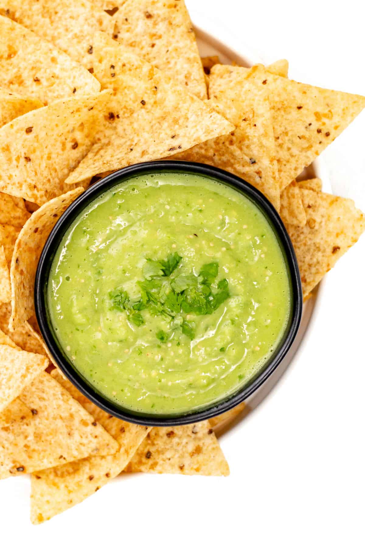 Overhead view of green salsa surrounded by tortilla chips.