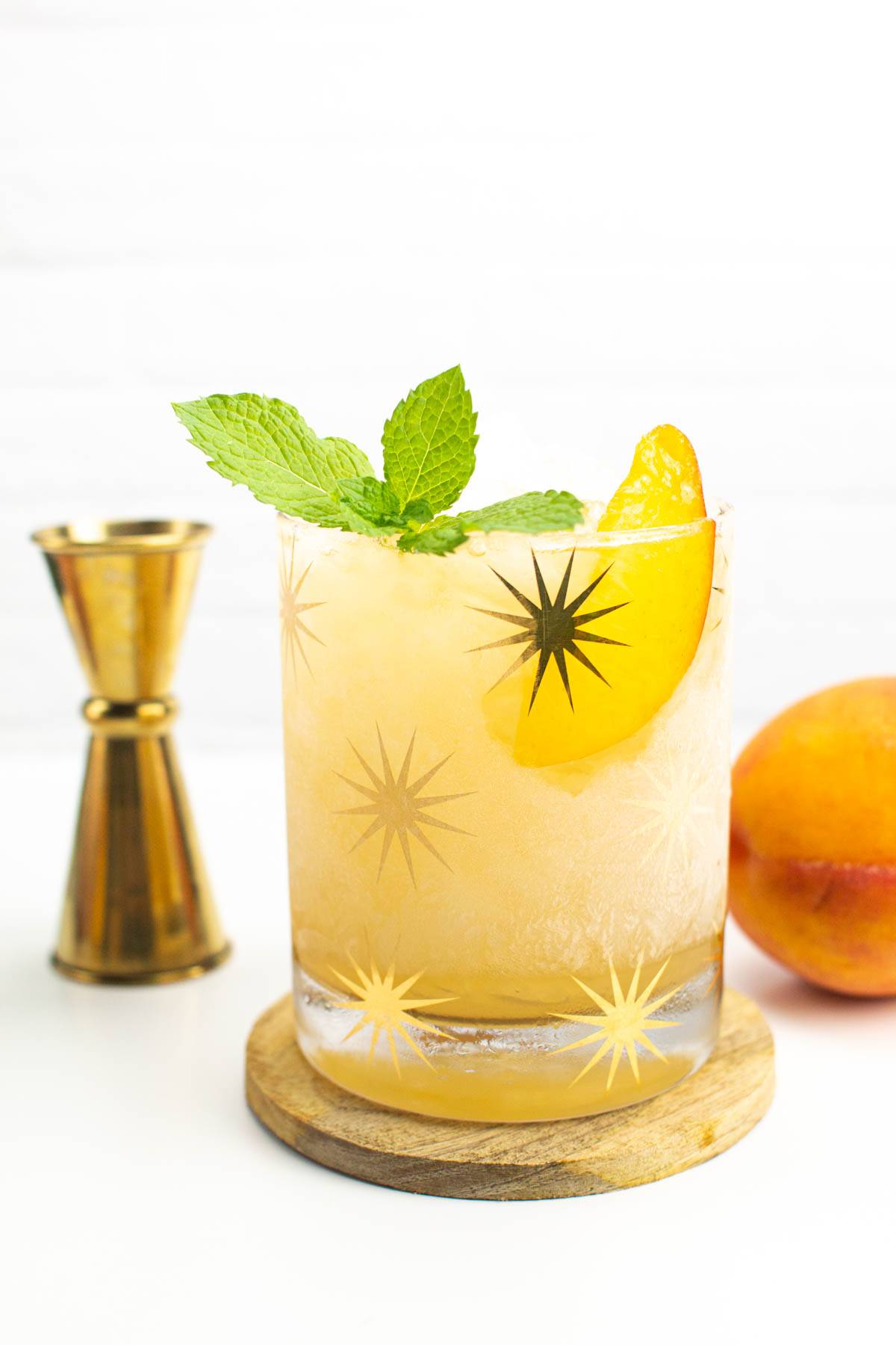 A yellow cocktail with a peach slice and a mint sprig.