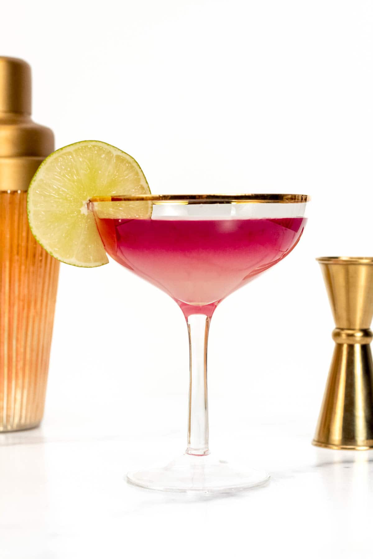 An ombré red margarita in a stemmed glass near gold bar tools.