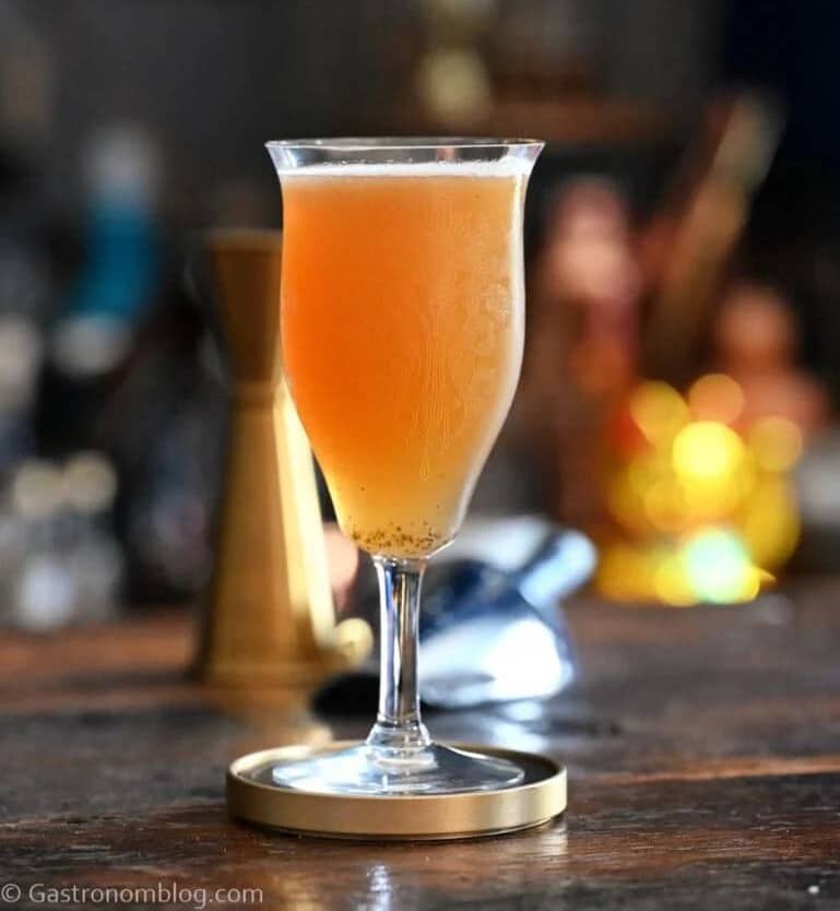 A light orange drink in a stemmed glass on a round coaster.